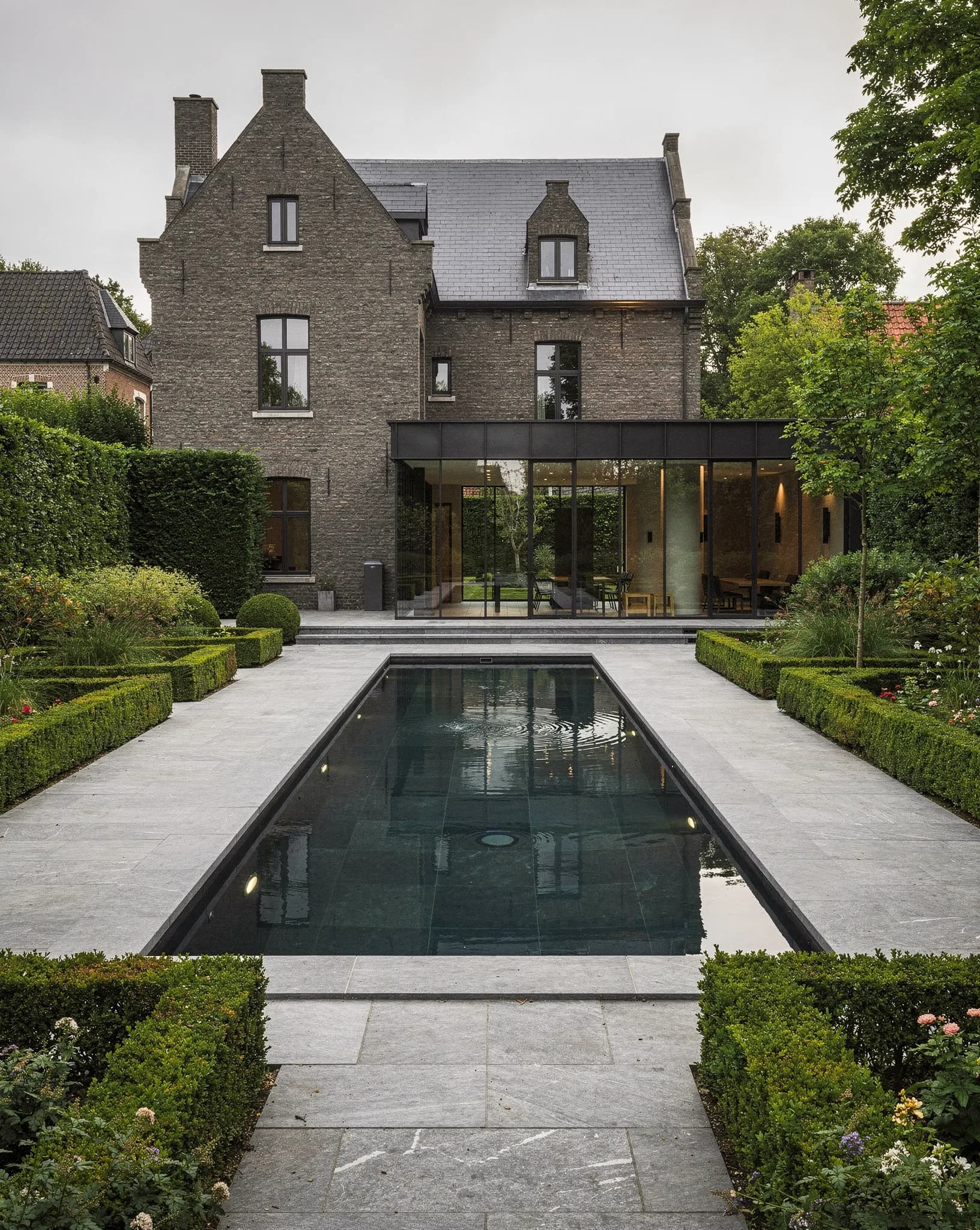 Architecturaal zwembad geïntegreerd in een gestructureerde Vlaamse tuin met geschoren hagen en blauwsteen