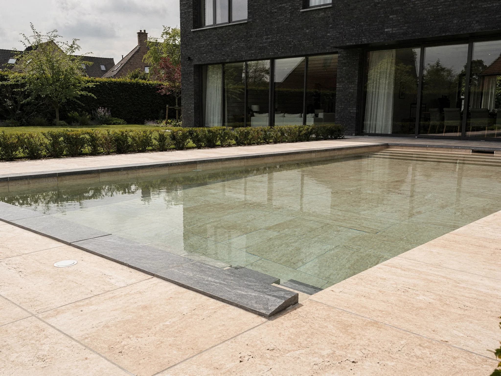 Conceptbeeld van een strak privaat zwembad met grootformaat tegels in travertijntint bij een moderne Vlaamse villa