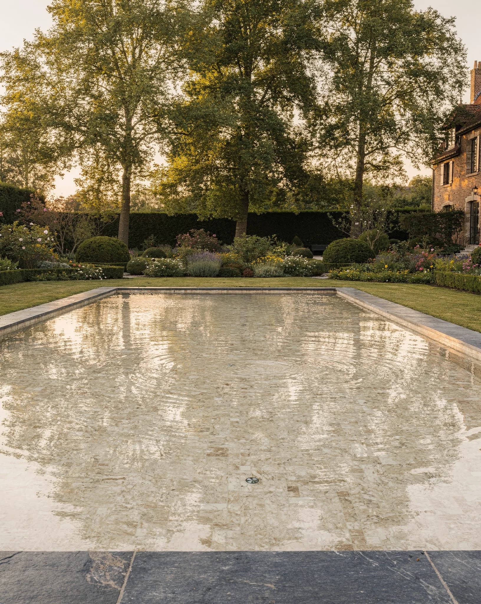 Conceptbeeld van een zwembad met licht mozaïek in champagnetinten en zacht glanzend water in een Vlaamse landelijke tuin