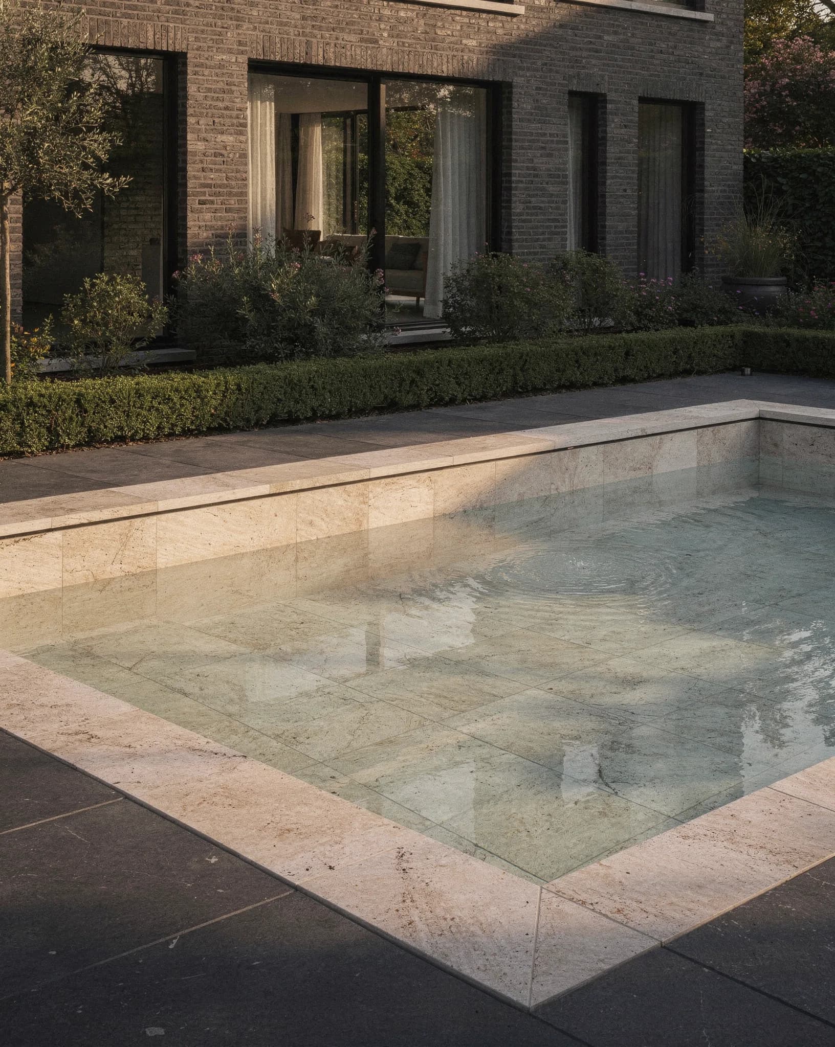 Conceptbeeld van een modern zwembad met grote zandkleurige natuurstenen tegels en helder water bij een hedendaagse Belgische villa